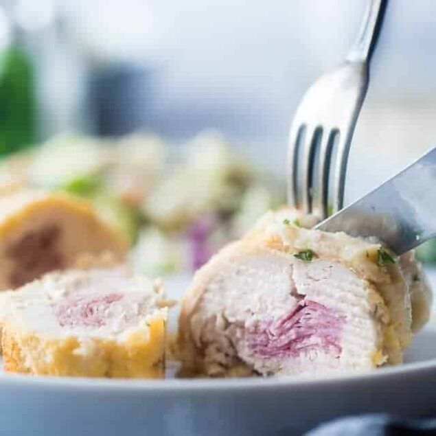 Close-up af et stykke fyldt kylling skåret med kniv og gaffel på en hvid tallerken.